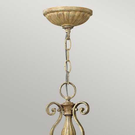 Elevate your space with the Carabel 3 Light Chandelier - Brushed Champagne, where elegant lighting is highlighted by an intricate metal fixture in a weathered gold hue that evokes brushed champagne. Its chain link configuration connects effortlessly to a round ceiling mount, all set against a gray backdrop.