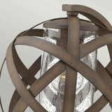 Introducing the Carson 1 Light Outdoor Small Wall Lantern in Vintage Iron: A glass cylinder envelops a bulb and is surrounded by gracefully curved metal bands, creating a spherical design. Its vintage iron finish lends an outdoor wall lantern a rustic, weathered charm.