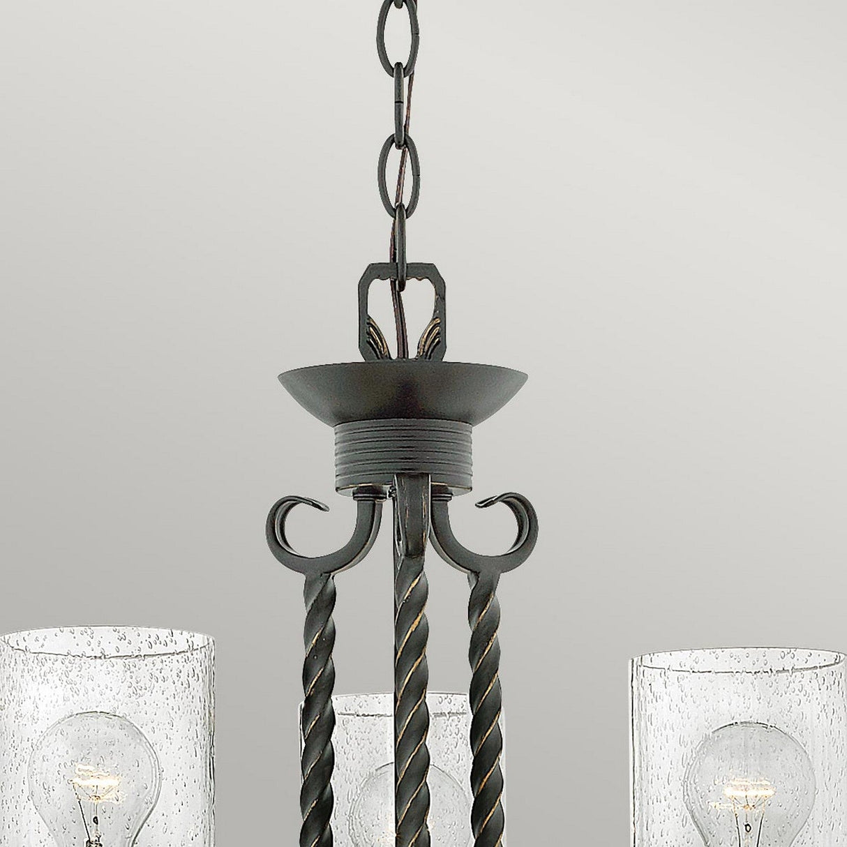 Close-up of the Casa 3 Light Chandelier - Black, showcasing a dark metal frame with twisted rods. It features two seedy glass shades, each housing a visible bulb. This elegant black chandelier is suspended from a chain against a neutral background.