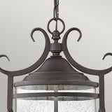 A close-up of the Casa 3 Light Outdoor Chain Lantern - Black, showcasing its ornate design. The lantern features clear seedy glass panels and elegant scrollwork details, highlighted by intricate pierced metalwork on top, hanging against a light gray background.
