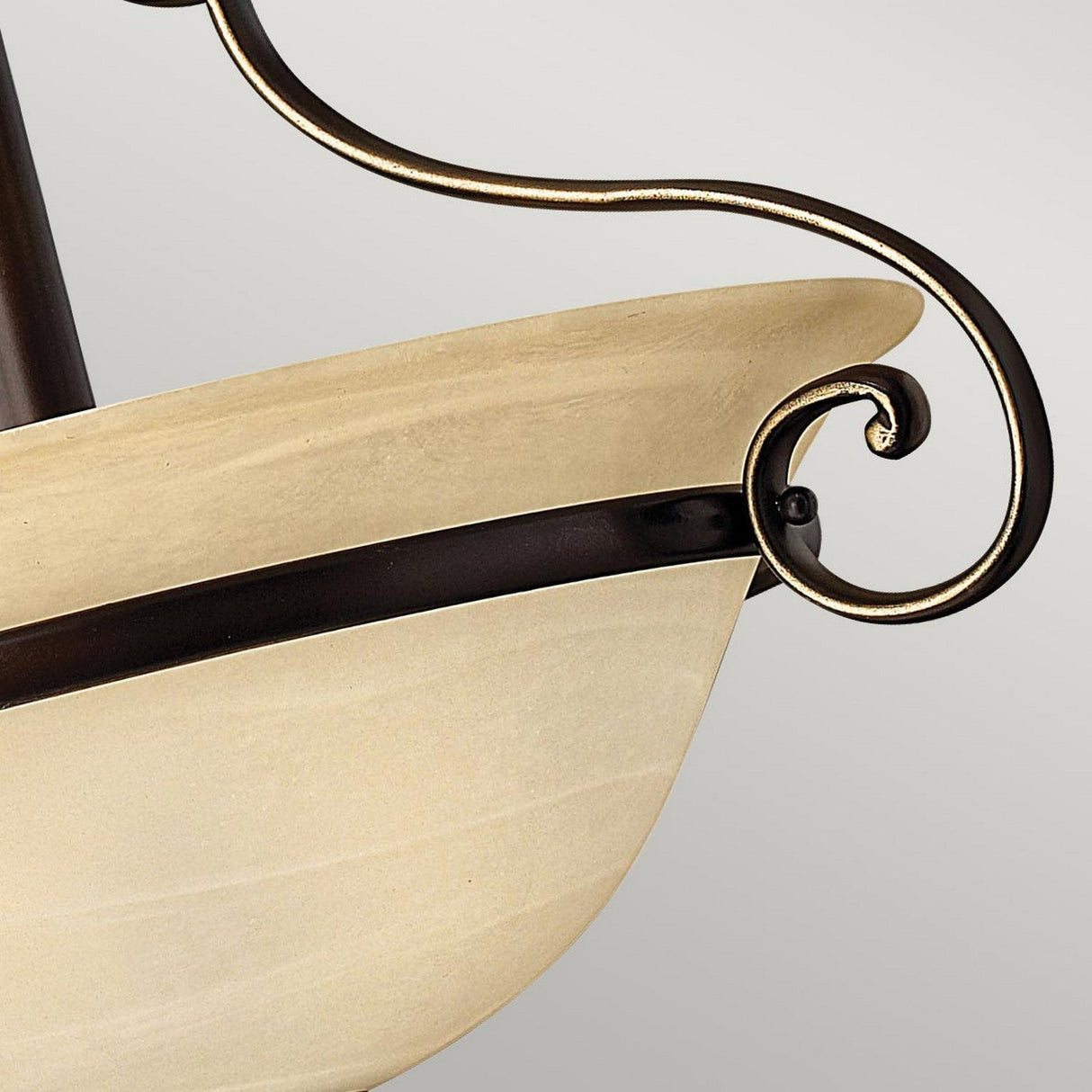 Close-up of the Cello 2 Light Semi Flush in an antique bronze finish, showcasing an ornate light fixture with a swirl design and a frosted faux alabaster glass bowl. The traditional fixture includes dark metal accents and a curved decorative metal arm, set against a plain, light gray background.