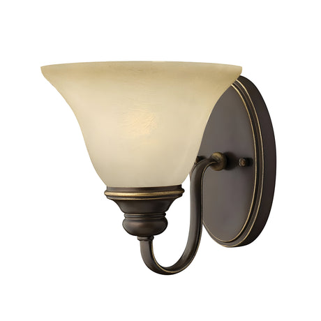 The Cello 1 Light Wall Light - Antique Bronze boasts a frosted glass shade that curves outward, infusing vintage charm. Mounted on an oval plate with elegant detailing, it creates a warm, inviting glow.