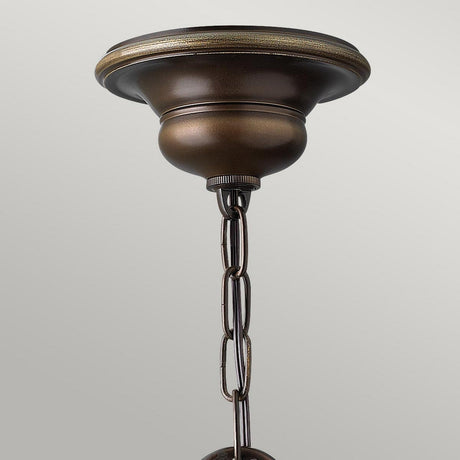 Close-up of the Cello 3 Light Chandelier in Antique Bronze, featuring a decorative mount and a short chain. The soft gray background accentuates the fixture's vintage metallic sheen and elegant design.