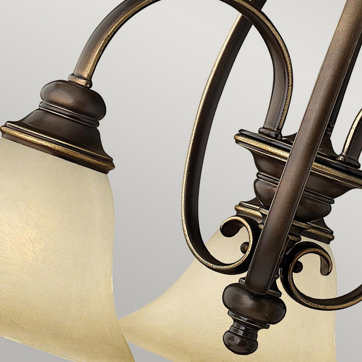 Close-up of the Cello 3 Light Chandelier in Antique Bronze with frosted glass shades. The elegant scrollwork and curved arms are highlighted against a neutral gray background.