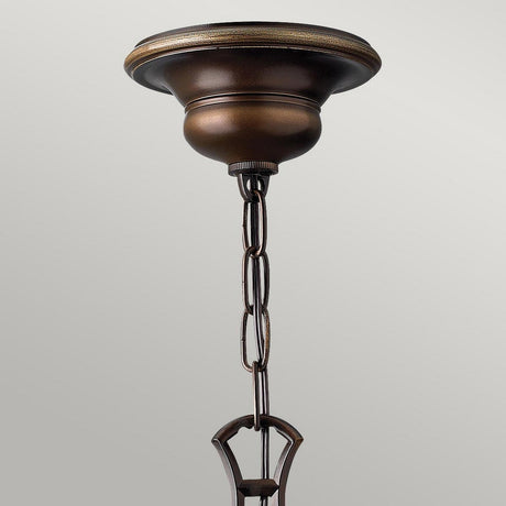The Cello 6 Light Chandelier in Antique Bronze features a decorative canopy and chain, echoing the elegance of a traditional chandelier. Its metal components have an antique bronze finish with a warm, dark tone and are complemented by vintage alabaster glass elements. The background is a neutral, light gray.