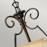 A detailed view of the Cello 9 Light Chandelier in antique bronze highlights its elegant scrollwork. The fixture is complemented by a cream-colored faux alabaster glass shade, adding classic and sophisticated charm against a neutral backdrop.