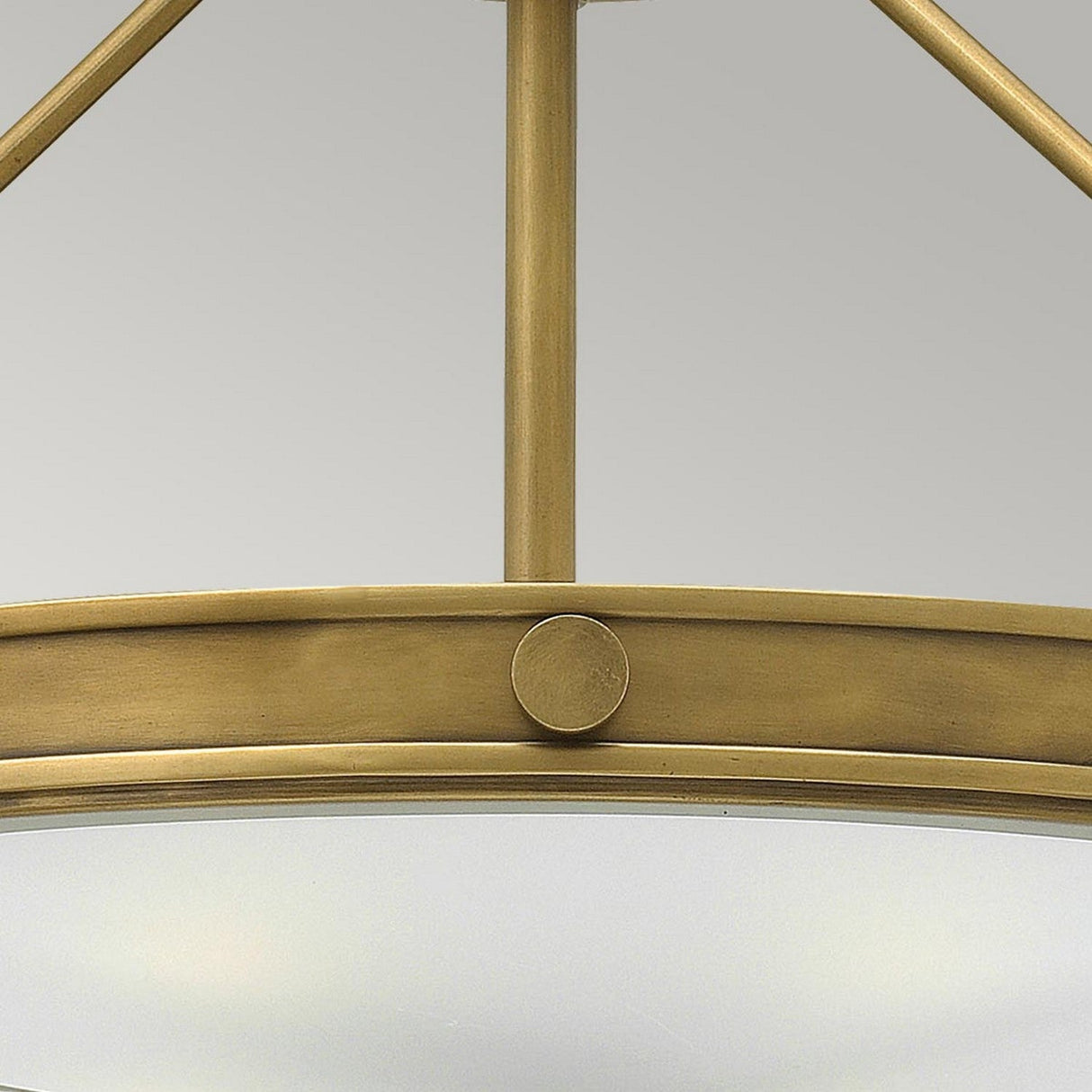 Close-up of the Collier 4 Light Large Semi Flush in Heritage Brass, showcasing its industrial-style mid-century silhouette with a circular frame and clean lines. The image emphasizes the metal's matte finish and a single decorative bolt, all set against a plain grey background.