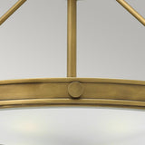 Close-up of the Collier 4 Light Large Semi Flush in Heritage Brass, showcasing its industrial-style mid-century silhouette with a circular frame and clean lines. The image emphasizes the metal's matte finish and a single decorative bolt, all set against a plain grey background.
