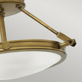 A close-up view of the Collier 3 Light Semi Flush ceiling light fixture in Heritage Brass showcases its frosted glass dome, accented by three visible metal supports that highlight its modern, minimalist design.