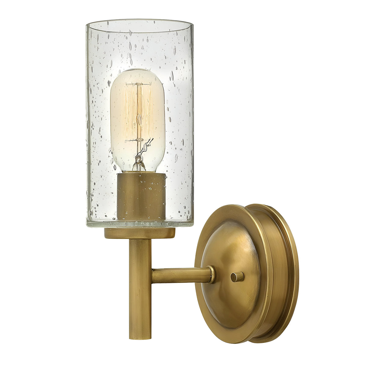 Introducing the Collier 1 Light Wall Light in Heritage Brass, featuring a clear cylindrical glass shade adorned with small decorative bubbles. It houses a vintage-style Edison bulb that emits a warm glow, complementing its vintage charm, while the base boasts a round, classic design.