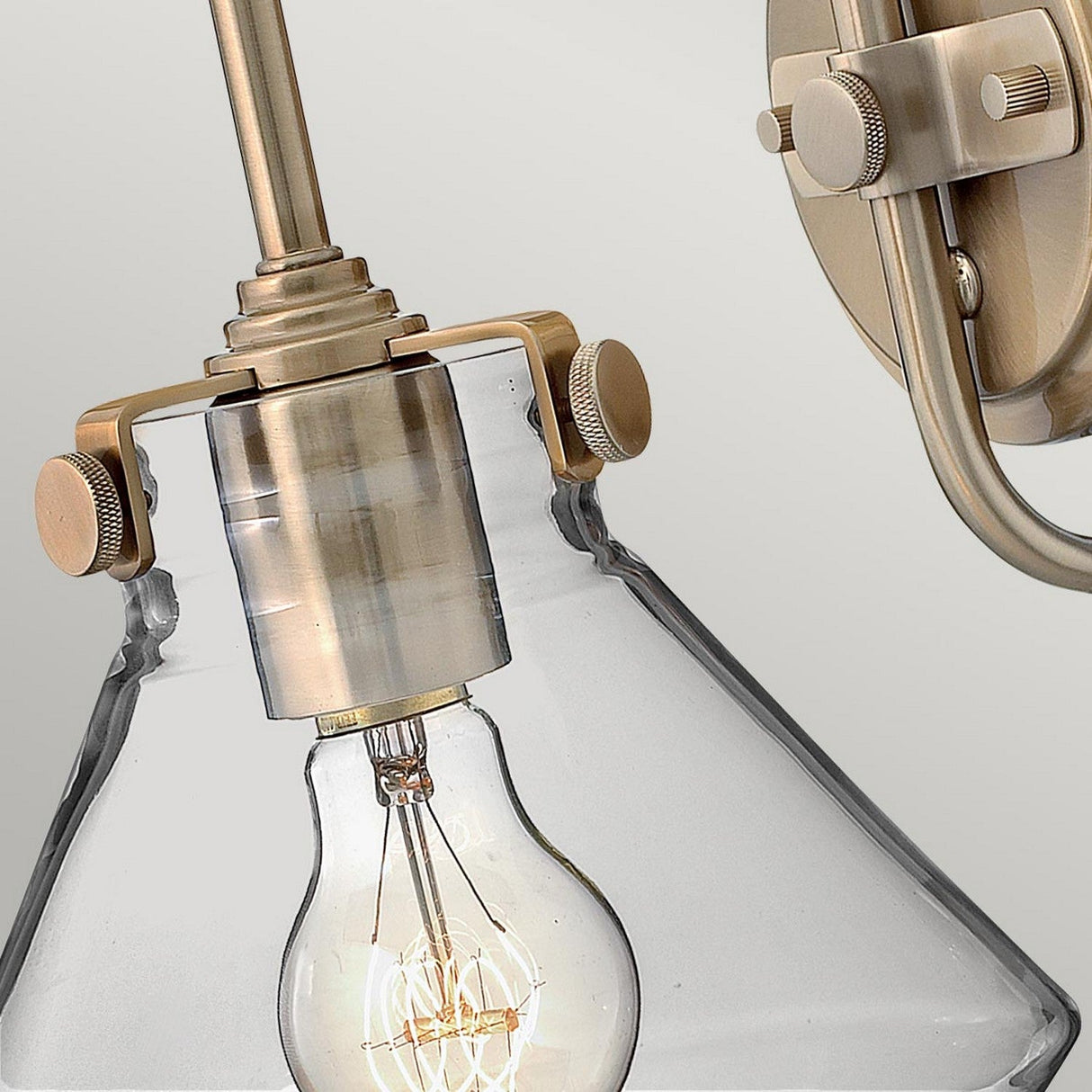 This close-up showcases the Congress 1 Light Clear Glass Wall Light in brushed caramel, highlighting an exposed bulb with a vintage design. Mounted on the wall with a decorative metal bracket, it emphasizes a minimalist yet elegant aesthetic while incorporating LED filament lamps for enhanced efficiency.