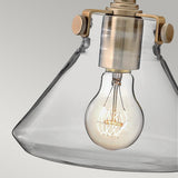 A Congress 1 Light Clear Glass Wall Light - Brushed Caramel features a vintage-style LED filament bulb with a visible filament, mounted within its clear glass fixture. The brushed caramel metallic accents contribute to a classic and industrial aesthetic, harmonizing modern technology with timeless allure against a neutral backdrop.