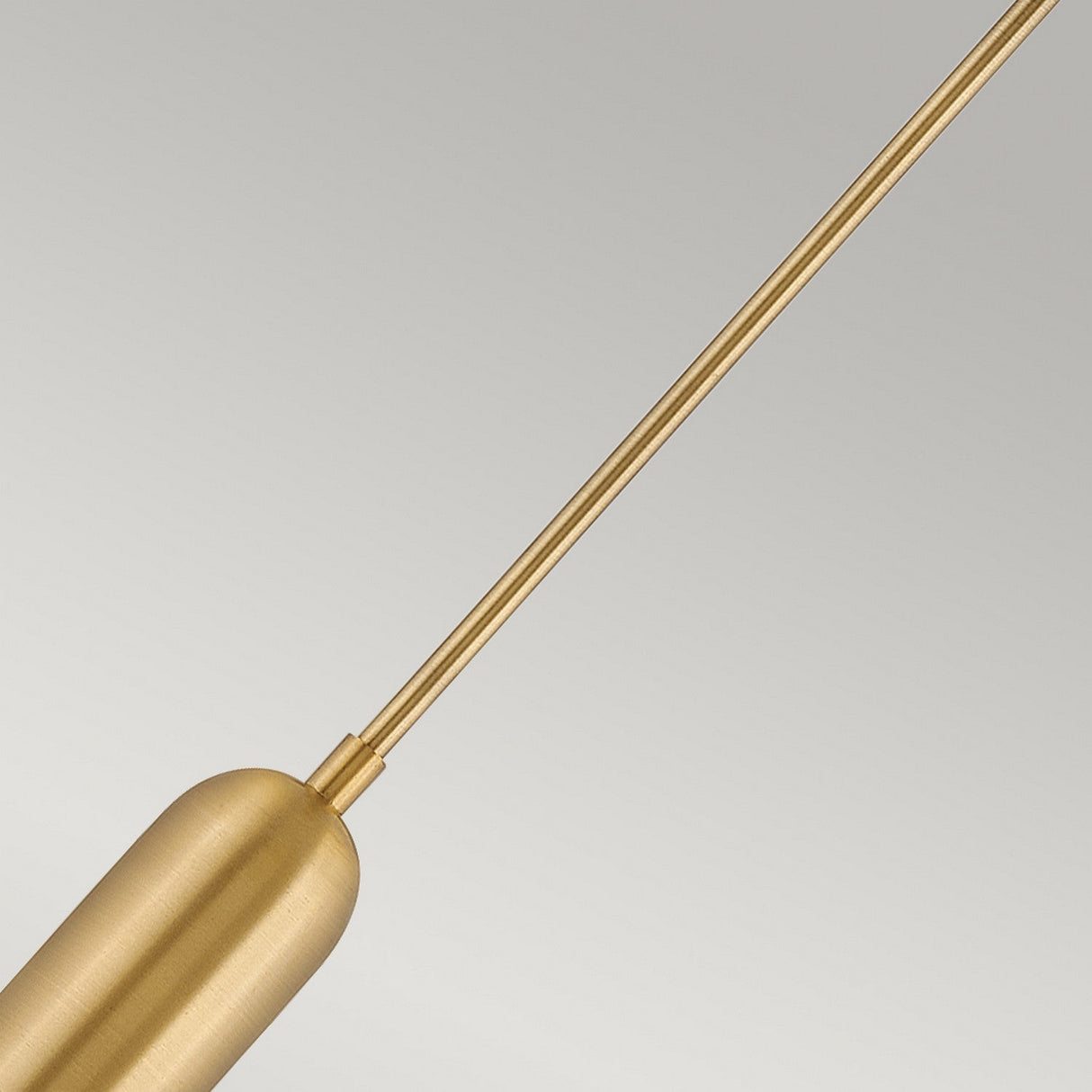 The Dax LED Mini Pendant in Heritage Brass features a cylindrical design suspended against a plain gray background. This energy-efficient light fixture showcases a sleek, minimalist aesthetic with a slender rod attached to the main body.