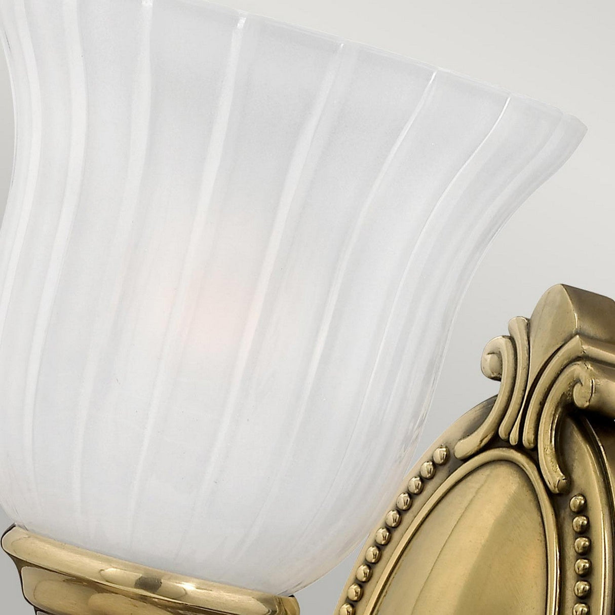 Close-up of the Francoise 1 Light Wall Light - Burnished Brass, featuring a frosted ribbed glass shade with an intricately detailed base. The light emits a warm, inviting glow.