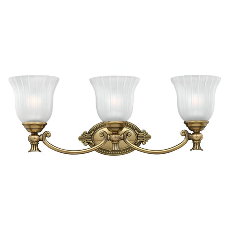The Francoise 3 Light Wall Light - Burnished Brass showcases a beautiful burnished brass design with three frosted ribbed glass shades elegantly shaped like tulips. It features decorative curves and is mounted on an ornate oval backplate, adding timeless elegance to any space.