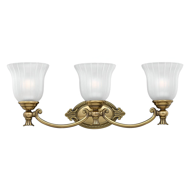 The Francoise 3 Light Wall Light - Burnished Brass showcases a beautiful burnished brass design with three frosted ribbed glass shades elegantly shaped like tulips. It features decorative curves and is mounted on an ornate oval backplate, adding timeless elegance to any space.