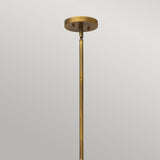 A close-up of the Fulton 13 Light Large Chandelier in bronze and brass, featuring a rod extending downward against a plain gray backdrop. The fixture boasts a minimalistic design with a smooth, metallic finish reminiscent of classic chandeliers.