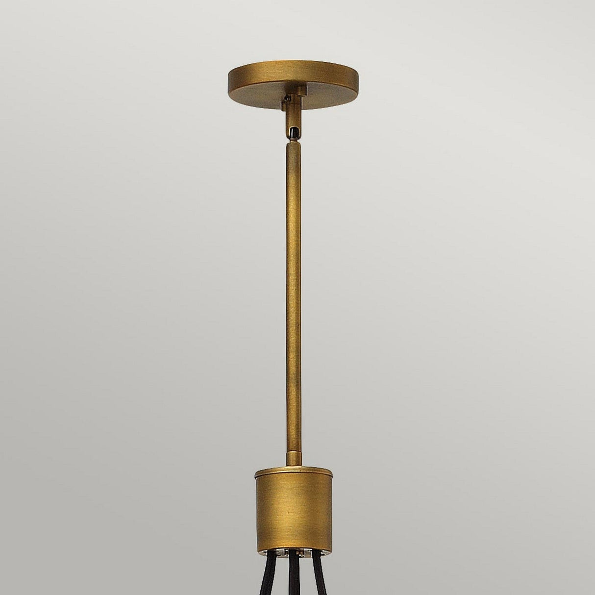 Positioned against a light gray background, a minimalist gold pendant light fixture with a cylindrical base mirrors the elegance of the Fulton 7 Light Chandelier - Bronze & Brass. It showcases a long, narrow rod linking the base to the ceiling mount, embodying minimalist design with bronze and brass accents.
