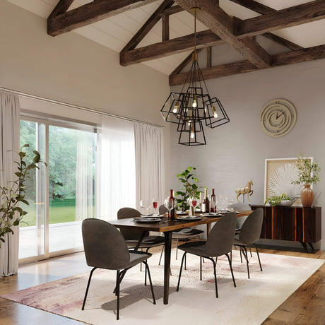 In a contemporary dining room, a wooden table set for six is surrounded by dark chairs. The table is elegantly adorned with wine glasses and red napkins. Above it, a Fulton 7 Light Chandelier in Bronze & Brass with a minimalist design hangs from the beamed ceiling. Large windows offer stunning views of the lush green outdoor space.