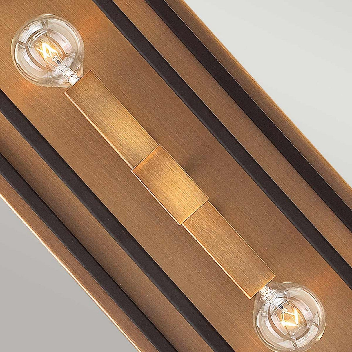 The Fulton 2 Light Wall Light - Bronze & Brass, with its modern rectangular design, presents two exposed light bulbs. It includes a sleek wooden frame finished in bronze and brass, complemented by black accents. Each bulb is placed at opposite ends to create a warm, ambient glow.