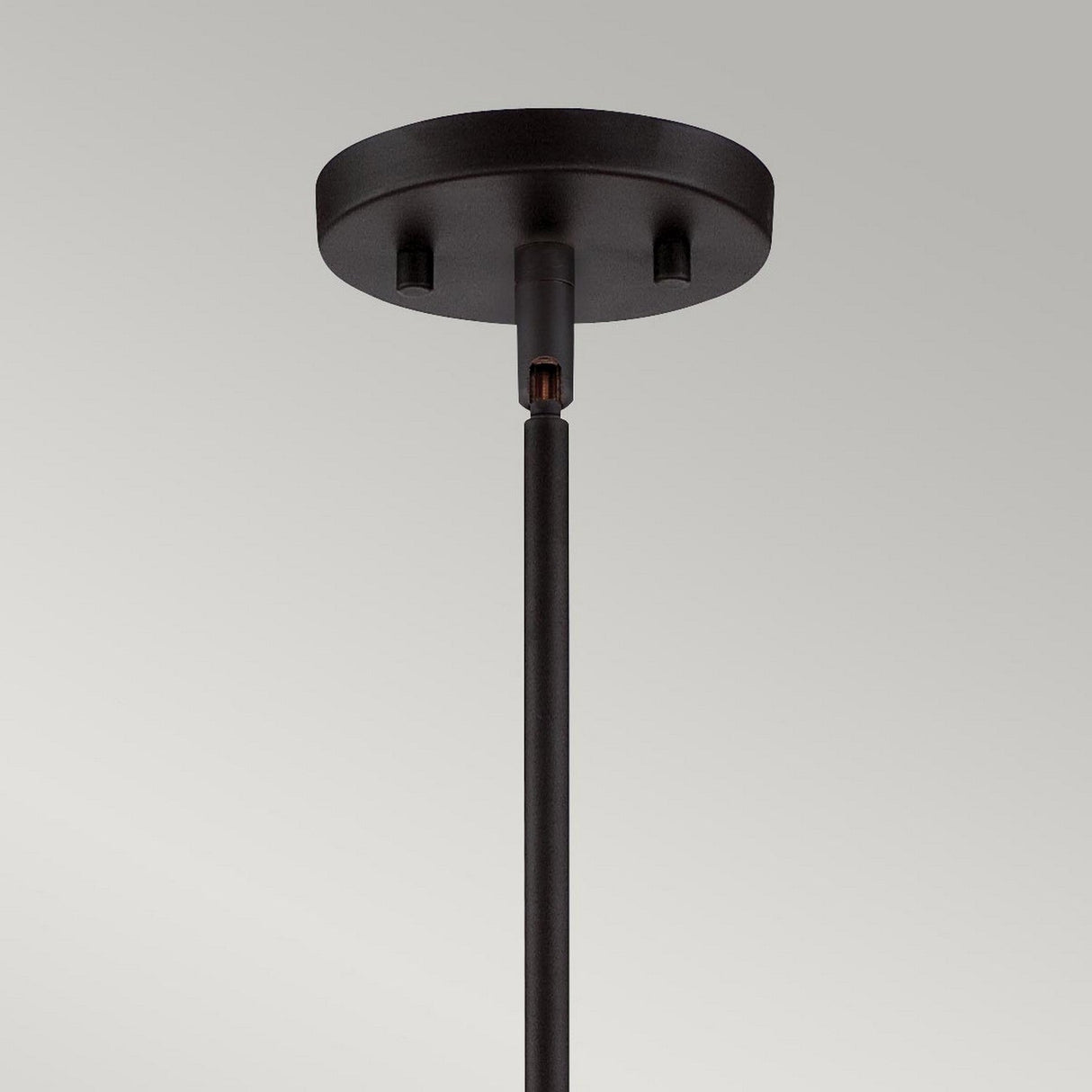 Close-up of the Gemma 3 Light Chandelier in vintage bronze, featuring a round base and single rod extending downwards for a contemporary style touch. The background is a plain off-white wall.