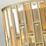 A detailed view of the Gemma-1 2 Light Wall Light - Gold shows a lampshade adorned with vertical rows of rectangular, transparent crystals in shades of yellow and beige. The amber pearl crystal accents capture and reflect light beautifully, casting a warm ambient glow against the gradient light gray background.