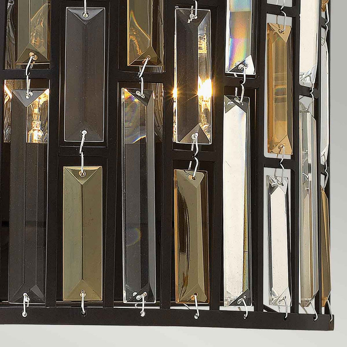 Close-up of the Gemma-1 2 Light Wall Light in vintage bronze, showcasing a contemporary sophistication with its black frame. Vertical rectangular glass prisms hang elegantly, creating a reflective and illuminated effect with a blend of golden and silver tones.