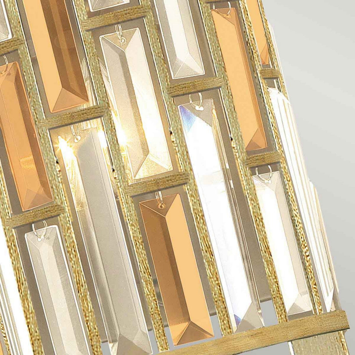 Close-up of the Gemma-2 2 Light Wall Light in gold, showcasing its geometric design with vertical, rectangular amber pearl crystal panels encased in a sumptuous gold frame. The light reflects off the crystals, producing a sparkling effect that exemplifies contemporary lighting fixtures.