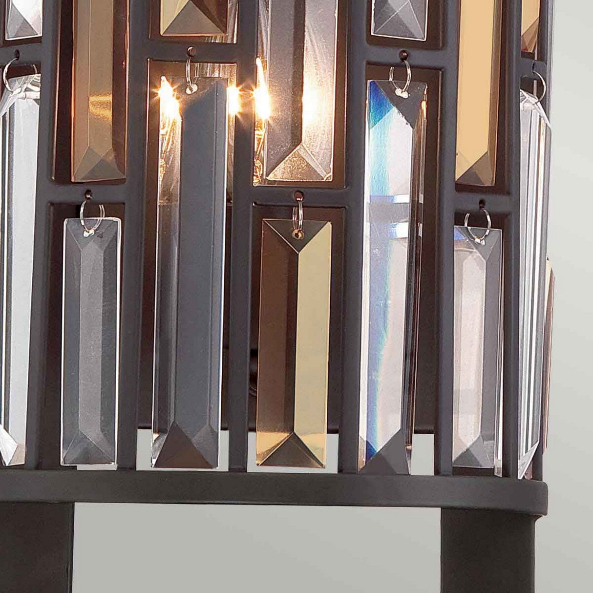 This elegant design, the Gemma-2 2 Light Wall Light - Vintage Bronze, showcases a close-up of its vintage bronze build, adorned with vertical rectangular crystal prisms. These clear and gold-hued crystals are set within a sleek black frame, allowing light to cast mesmerizing reflections as it shines through.