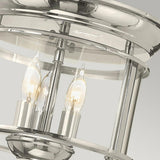 Close-up of the Gentry 3 Light Flush - Polished Nickel, a ceiling light that combines modern and traditional design elements with three candle-style bulbs encased in a cylindrical frame, set against a neutral background.