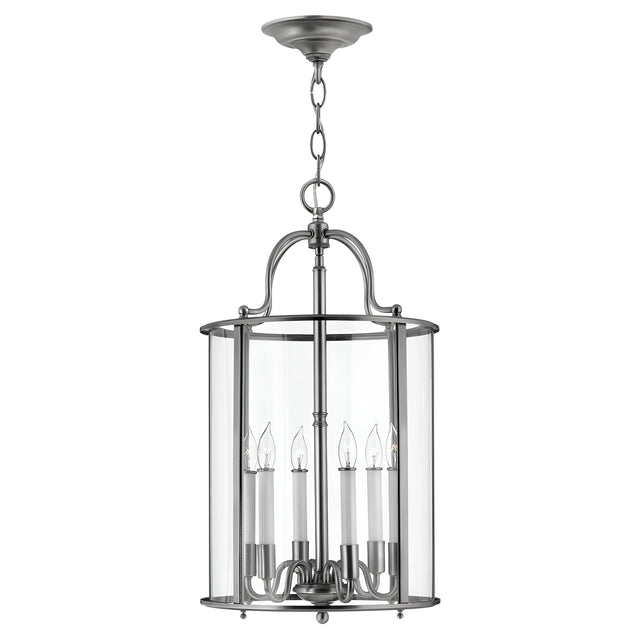 The Gentry 6 Light Large Pendant - Silver is a modern masterpiece, showcasing a cylindrical glass enclosure complemented by a brushed metal frame. It features six candle-style bulb holders inside, making it a stunning contemporary lighting fixture that hangs elegantly from a chain and circular ceiling mount.