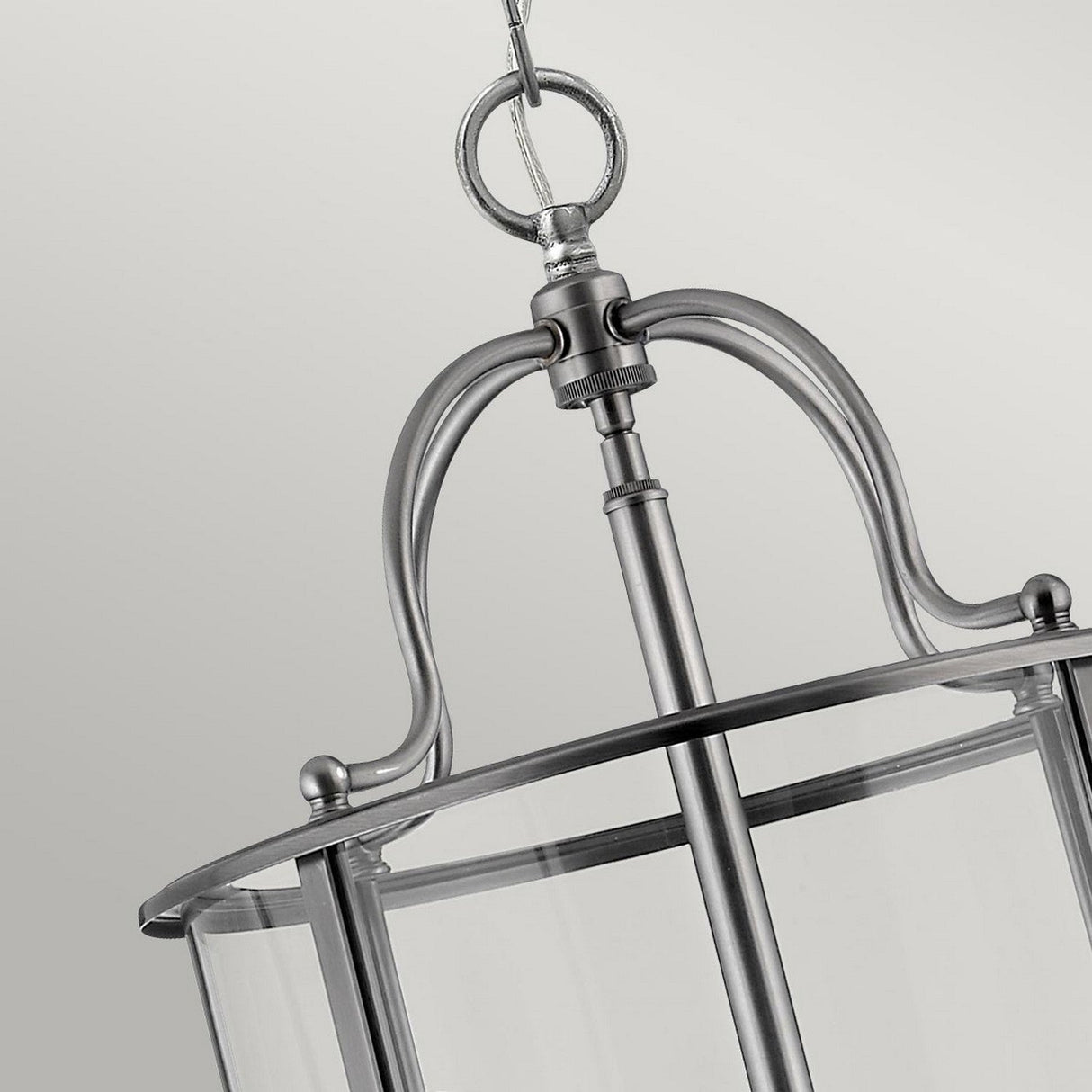 Close-up of the Gentry 6 Light Large Pendant in silver. This elegant design showcases a circular frame adorned with glass panels, suspended gracefully by a chain. Its brushed metal finish accentuates the contemporary aesthetic. Set against a plain, soft gray backdrop, it highlights this striking piece of modern lighting design.