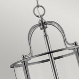 Close-up of the Gentry 6 Light Large Pendant in silver. This elegant design showcases a circular frame adorned with glass panels, suspended gracefully by a chain. Its brushed metal finish accentuates the contemporary aesthetic. Set against a plain, soft gray backdrop, it highlights this striking piece of modern lighting design.