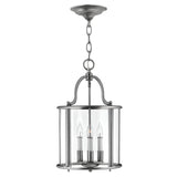 The Gentry 4 Light Medium Pendant - Silver features a brushed metal finish and clear bent glass panels. Inside, four candle-style sockets hold clear bulbs, all elegantly encased. Suspended by a chain, this sophisticated silver pendant showcases a gracefully curved design that exudes timeless elegance.
