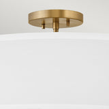 A close-up of the Graham 4 Light Duo-Mount Pendant/Semi-Flush reveals a white cylindrical shade accompanied by lacquered brass mounting. Its minimalist design radiates modern elegance, seamlessly enhancing the neutral background while capturing the sophisticated style of this lighting fixture.