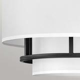 A detailed view of the Graham 3 Light Duo-Mount Pendant/Semi-Flush - Black highlights its contemporary ceiling light design featuring a white cylindrical shade complemented by black metal details. The bright faux parchment forms streamlined, layered circular elements set against a neutral background, achieving a minimalist aesthetic.