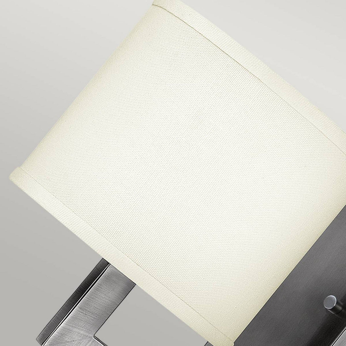 Close-up of the Hampton 1 Light Wall Light, showcasing its ivory drum shade and antique nickel metal base against a light gray background.