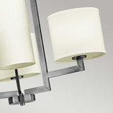 Close-up of the Hampton 4 Light Chandelier, featuring a modern design with four cylindrical ivory fabric lampshades in antique nickel, set against a gray background.