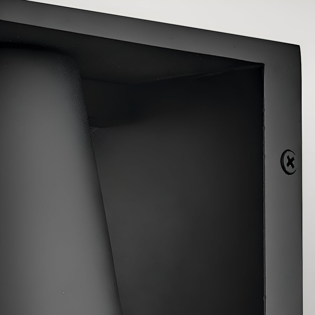 Close-up of the Coastal 1 Light Small Outdoor Wall Lantern in Textured Black, showing its smooth, curved design with a recessed corner and visible screw on the right edge, set against a plain light background.
