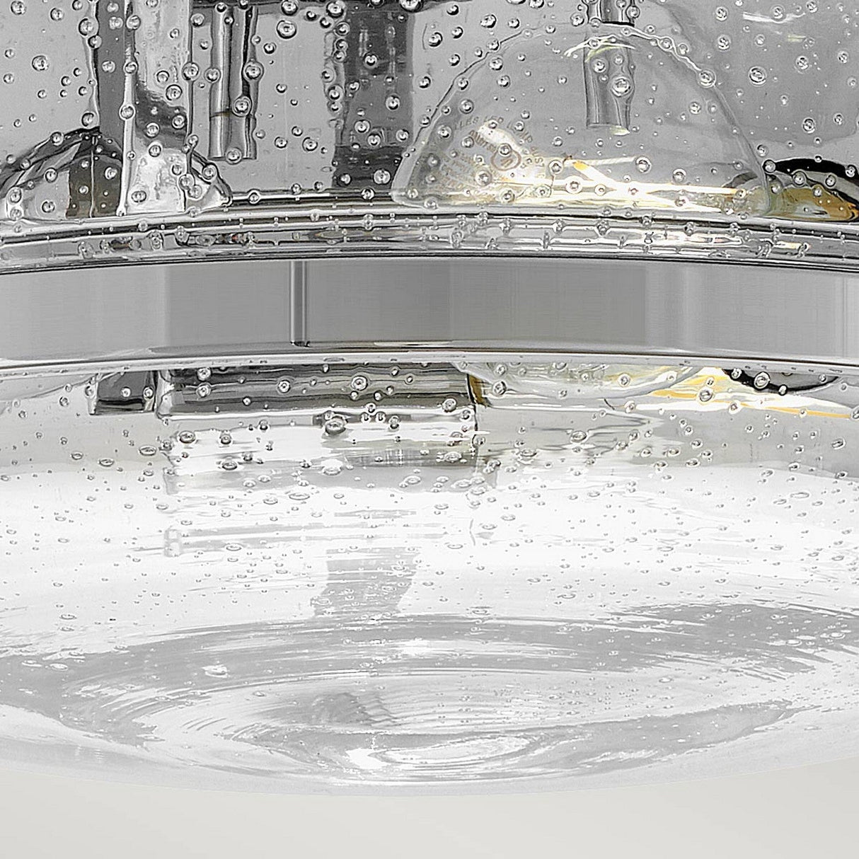 Close-up of a glass filled with carbonated water, bubbles rising to the surface. In the background, there's a glimpse of another glass partially visible beneath the Harper 3 Light Flush - Polished Chrome With Clear Seeded Glass fixture. The scene is illuminated from above, accentuating the clarity and texture of the water and bubbles.