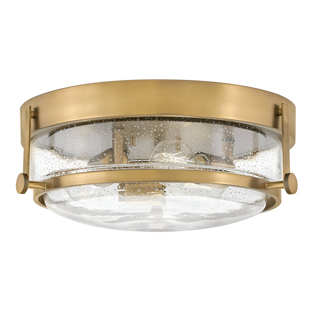 Introducing the Harper 3 Light Flush fixture, featuring a Heritage Brass frame and clear seeded glass. The bubble-textured glass showcases visible bulbs, creating a sleek design that elegantly merges modern and retro elements.