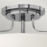 A close-up of the Harper 3 Light Small Semi Flush fixture showcases its polished chrome finish and modern design. Featuring a circular base with elegantly curved supports attached to the main frame, this stylish piece reflects light beautifully against a neutral background, enhanced by opal etched glass.