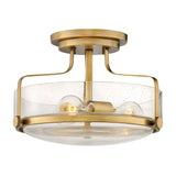 The Harper 3 Light Small Semi Flush in Heritage Brass features two exposed bulbs and a clear seeded glass shade with subtle speckles, mounted on a short brass stem.