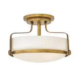 The Harper 3 Light Small Semi Flush in Heritage Brass features an opal etched glass shade with a circular design. Its modern and elegant look is accentuated by two curved metal supports connecting the base to the shade.