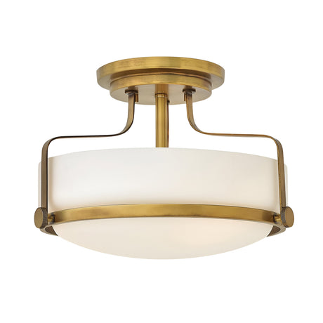 The Harper 3 Light Small Semi Flush in Heritage Brass features an opal etched glass shade with a circular design. Its modern and elegant look is accentuated by two curved metal supports connecting the base to the shade.