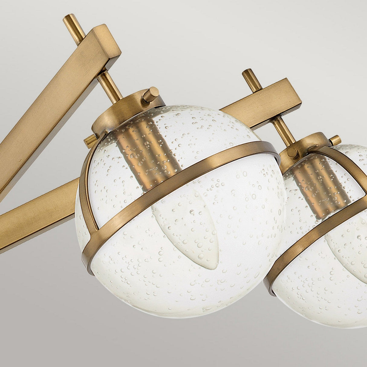 A close-up of the Hollis 5 Light Semi Flush – Heritage Brass With Clear Seeded Glass showcases its modern design with clear seeded glass shades featuring small bubble-like textures. The metallic frame, finished in a striking heritage brass, includes multiple rods elegantly connecting to the ceiling.