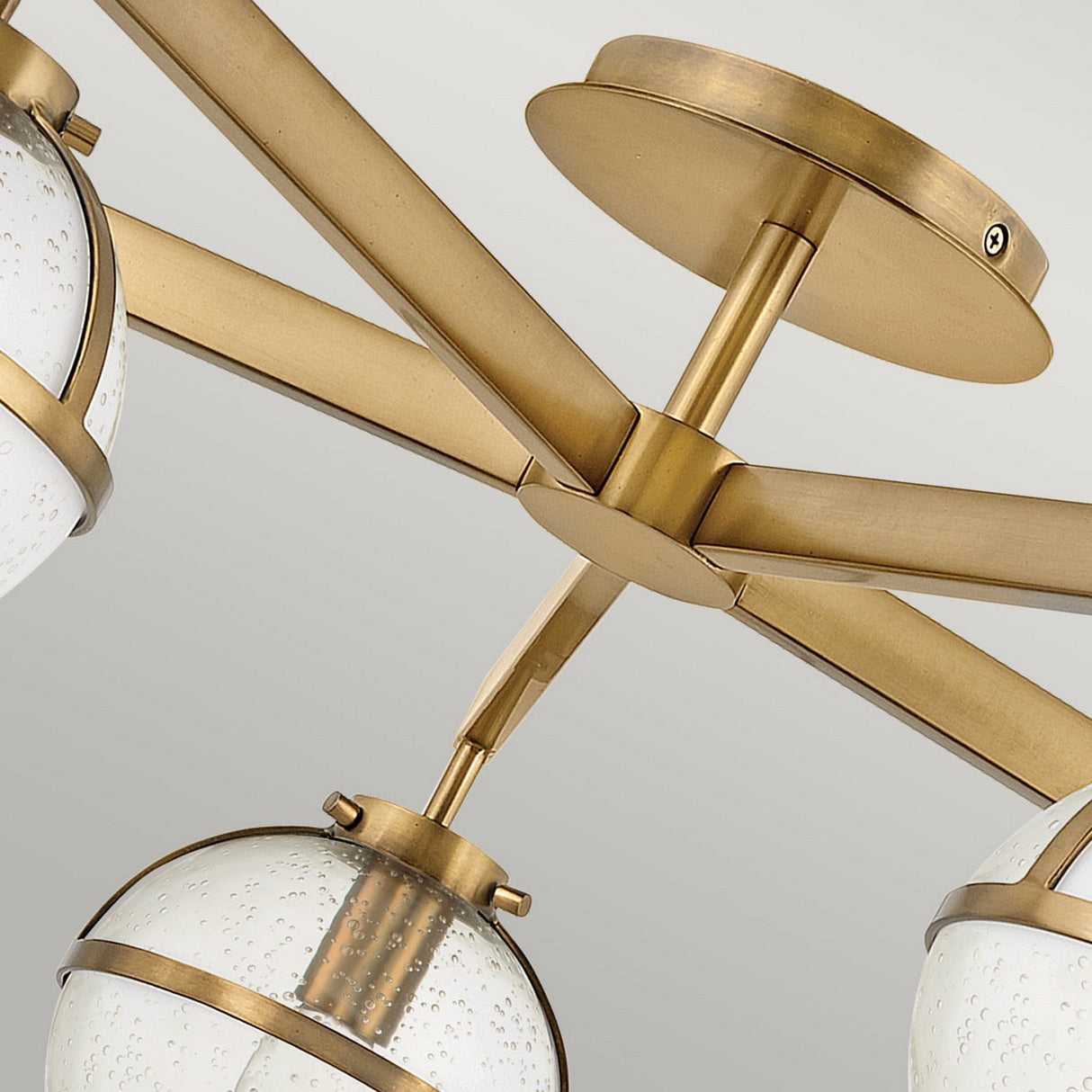 Close-up of the Hollis 5 Light Semi Flush in Heritage Brass. This fixture features multiple arms, each supporting a spherical shade of clear seeded glass. Both the ceiling mount and connecting rods are crafted in matching brass, creating a cohesive design.