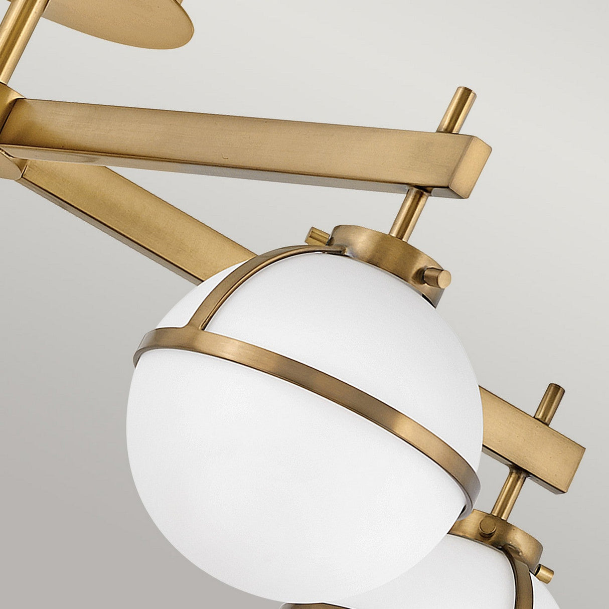 Close-up of the Hollis 5 Light Semi Flush in heritage brass, highlighting its opal etched glass lampshades. The design exhibits intersecting rods and an elegant, minimalist aesthetic set against a light gray background.