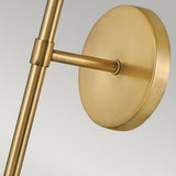 A detailed view of the Hollis 1 Light Wall Light in Heritage Brass reveals its round base and cylindrical arm, embodying Art Deco sophistication. The matte finish perfectly complements the opal glass shade, all set against a light gray gradient.