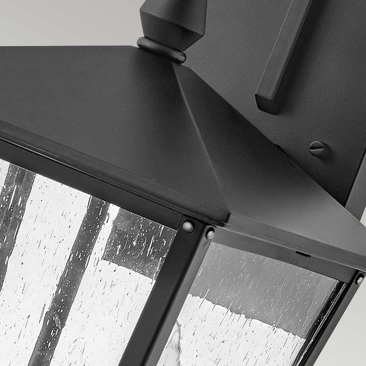 Close-up of the sleek Huntersfield Outdoor 2 Light Medium Wall Lantern in black, featuring a pyramid-shaped top and clear glass panels. The textured glass simulates the appearance of rainfall, enhancing your outdoor lighting setup with elegance.